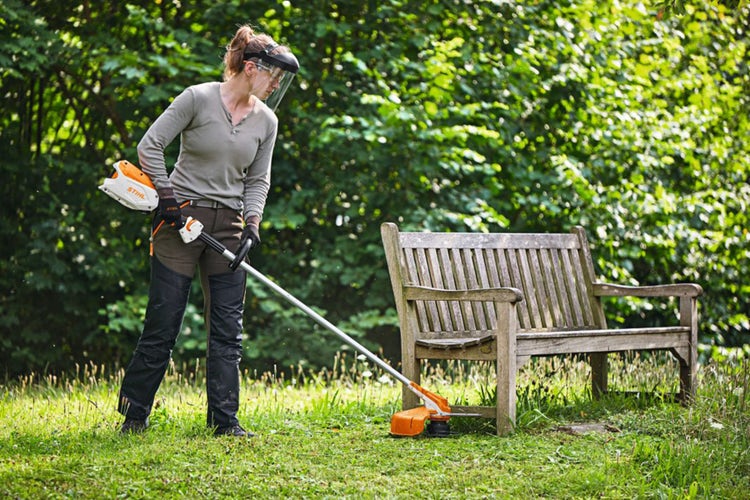 Frau mäht mit STIHL FSA 86 R Motorsense um eine Holzbank herum