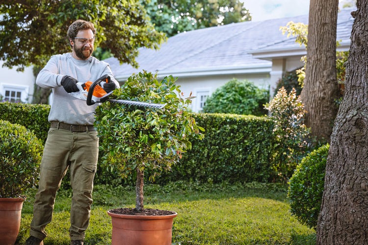 Ein Mann schneidet seinen Strauch mit der STIHL HSA 40