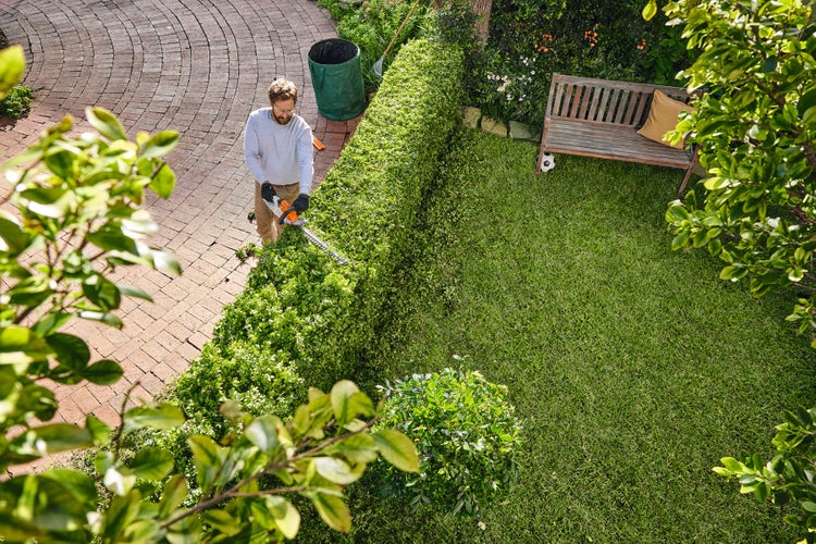 Ein Mann schneidet seine Hecke mit der STIHL HSA 40