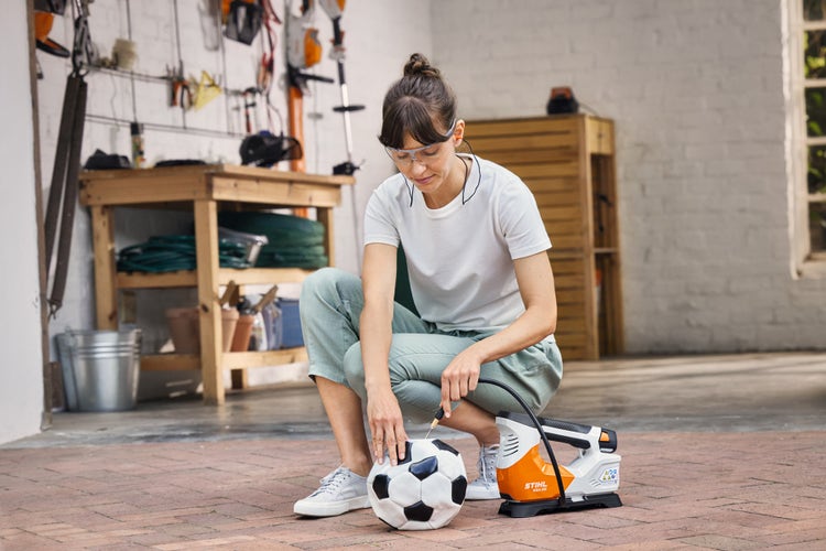 Eine Frau pumpt einen Fußball mit dem STIHL KOA 20 auf